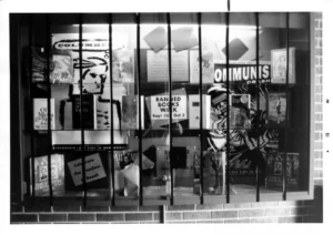 A barred glass display window featuring banned books and posters about censorship. The central sign promotes Banned Books Week (Sept 26 - Oct 3), with slogans like "Celebrate the Freedom to Read."