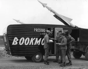 A black and white photo shows a military bookmobile, labeled "PRESIDIO BOOKMOBILE," with several soldiers standing around it. In the background, a missile or rocket points skyward.